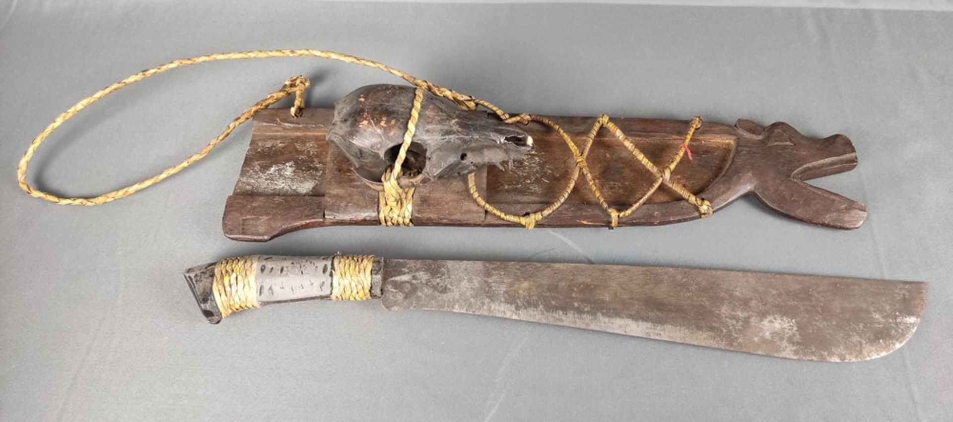 Machete, in wooden scabbard with carved animal head, mounted animal skull, brown lacquered, straw