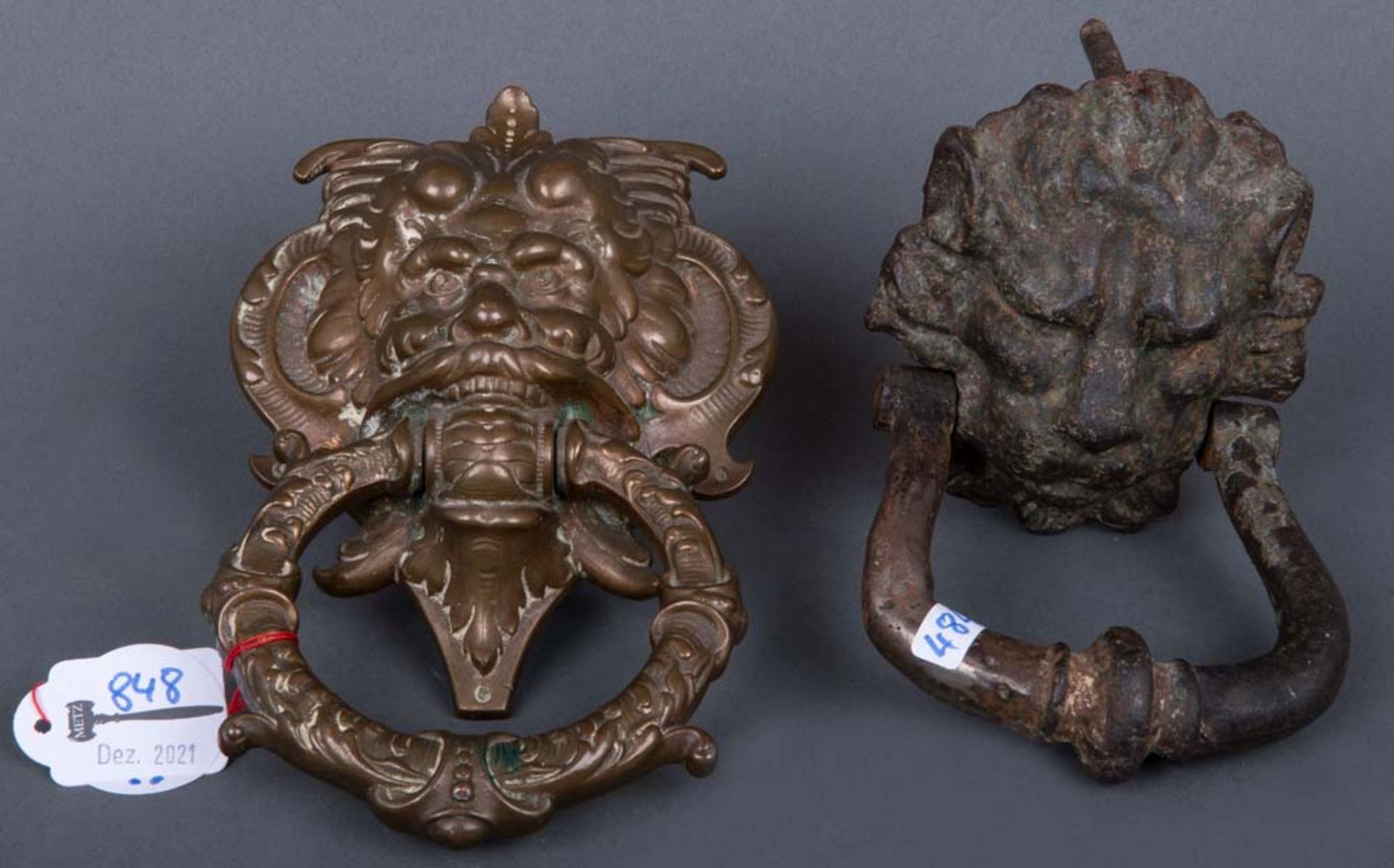 Zwei Türklopfer. Deutsch 18. bzw. 20. Jh. In Maskaronen- bzw. Löwenkopfform. Bronze / Eisen, H=
