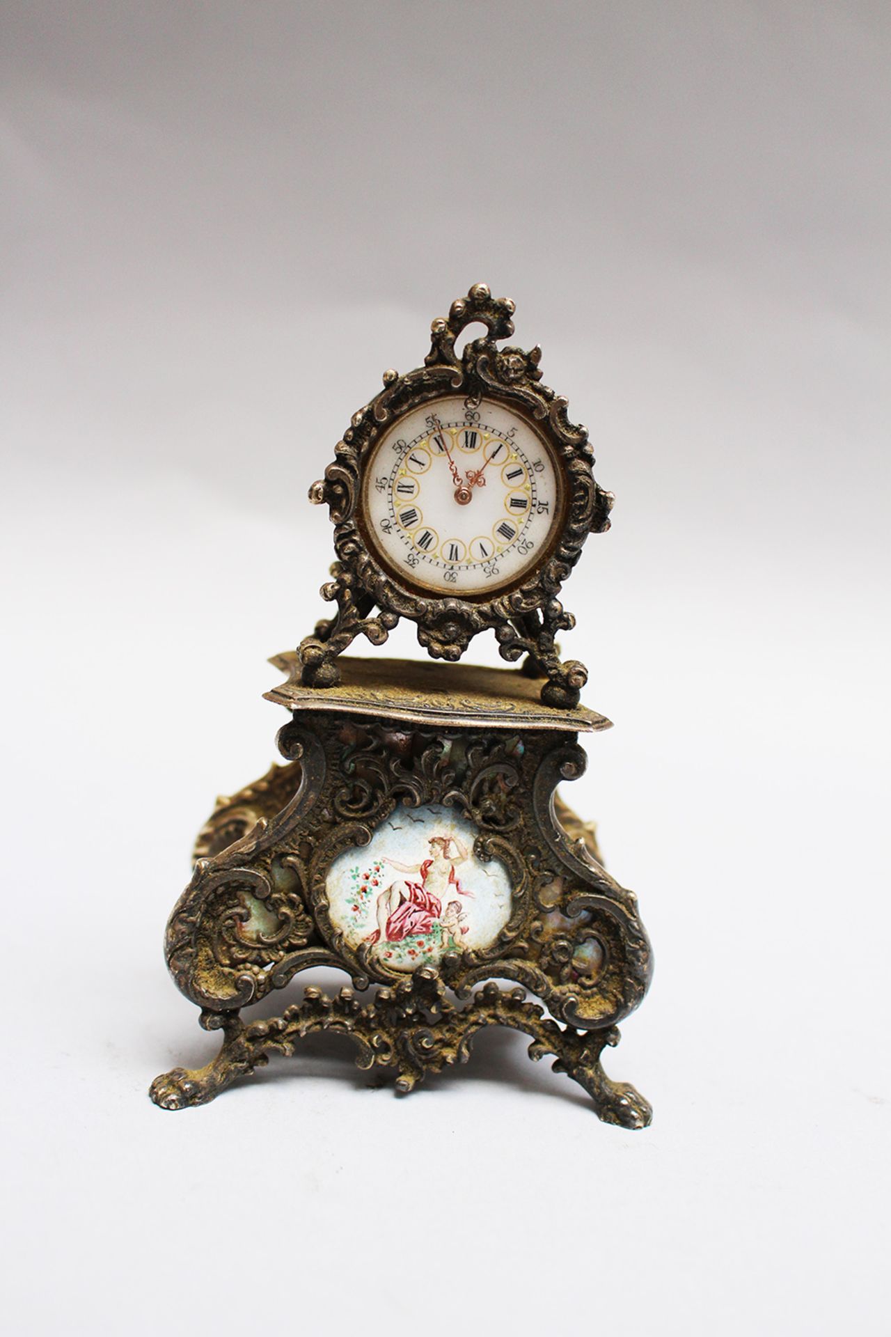 Silver miniature clock, in baroque from , inside gilted, with enamel dial and painting, open