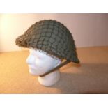 A BRITISH ARMY STEEL HELMET WITH LINING AND NET COVER TOGETHER WITH A CAMOFLAGE COVER