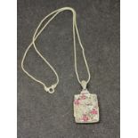 A SILVER NECKLACE WITH AN ORNATE LOCKET WOTH RED STONES AND CLEAR STONE CHIPS IN A DELICATE FLORAL