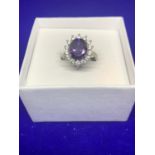 A SILVER RING MARKED 925 WITH A LARGE CENTRE PURPLE STONE SURROUNDED BY FOURTEEN CLEAR STONES IN A