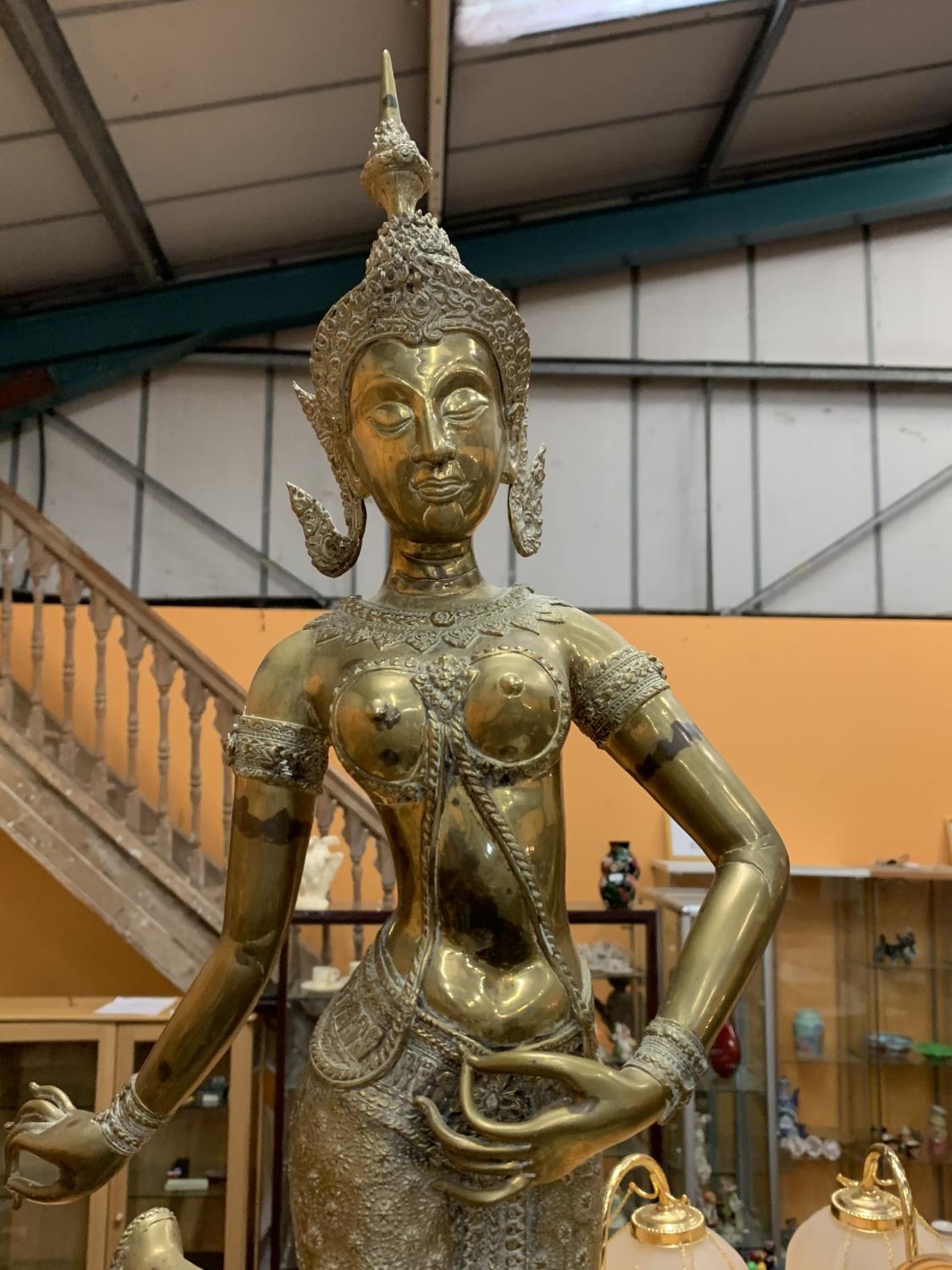 A LARGE BRASS STATUE OF A ORIENTAL TEMPLE DANCER ON A WOODEN PLINTH - HEIGHT 79CMS
