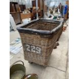 A LARGE VINTAGE WICKER LAUNDRY TROLLEY ON METAL WHEELS