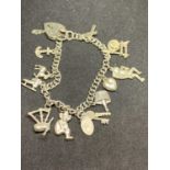 A SILVER CHARM BRACELET WITH ELEVEN CHARMS TO INCLUDE KEYS, BAGPIPES, ANCHOR, CROSS, SPINNING
