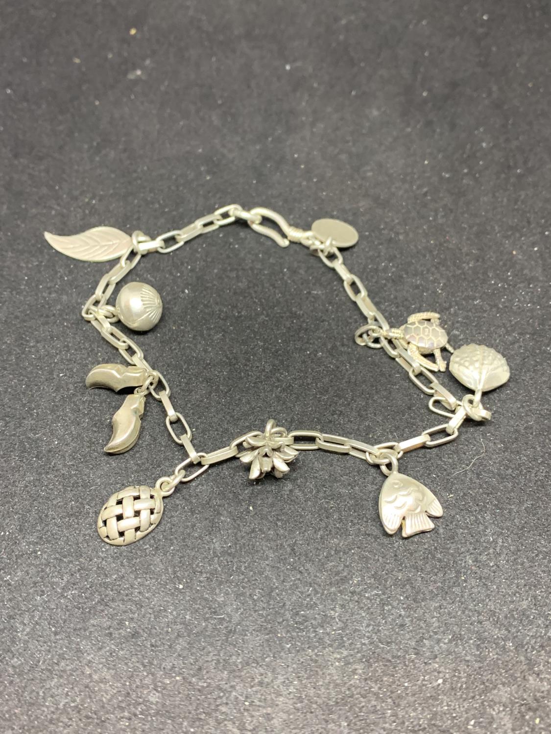 A SILVER CHARM BRACELET WITH NINE CHARMS TO INCLUDE CLOGS, FEATHERS, TURTLE, FISH, SHELL ETC