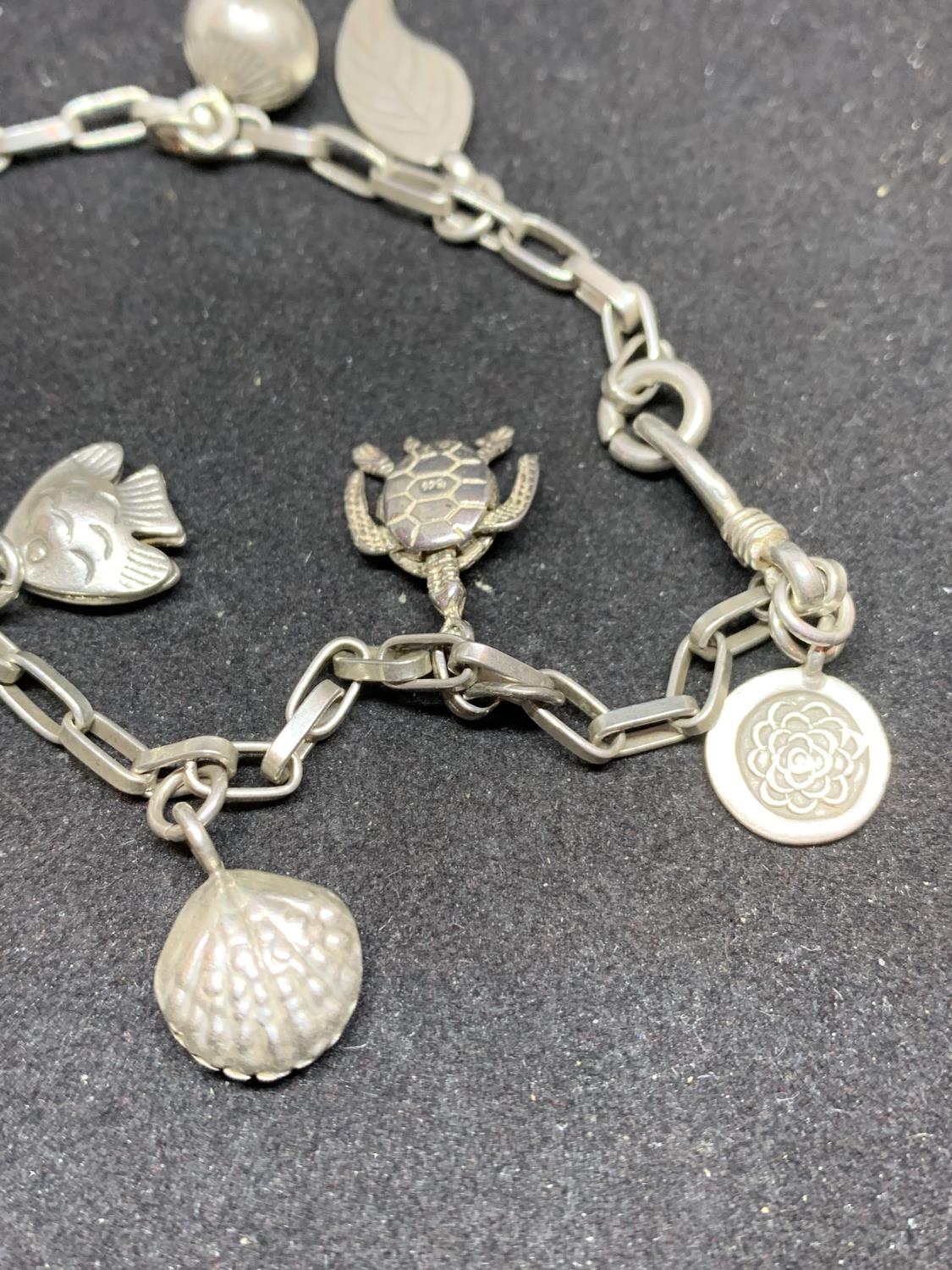A SILVER CHARM BRACELET WITH NINE CHARMS TO INCLUDE CLOGS, FEATHERS, TURTLE, FISH, SHELL ETC - Image 4 of 4