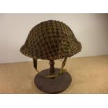 A BRITISH WORLD WAR II PERIOD STEEL HELMET WITH CAMOFLAGE COVER