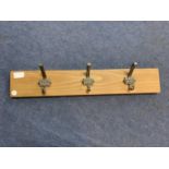 A SET OF THREE COAT HOOKS 'MADE IN BRITAIN' MOUNTED ON A WOODEN BACKING