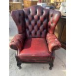 AN OXBLOOD WINGED BUTTON BACK FIRESIDE CHAIR ON CABRIOLE LEGS