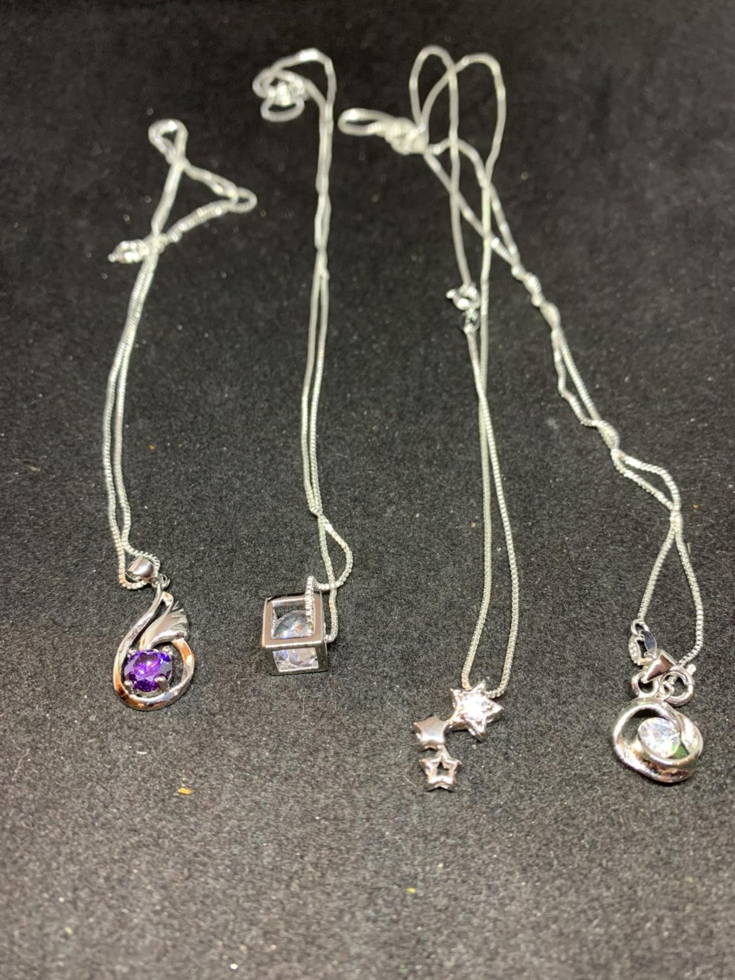 FOUR SILVER NECKLACES WITH CLEAR STONE PENDANTS TO INCLUDE A CUBE, STARS ETC