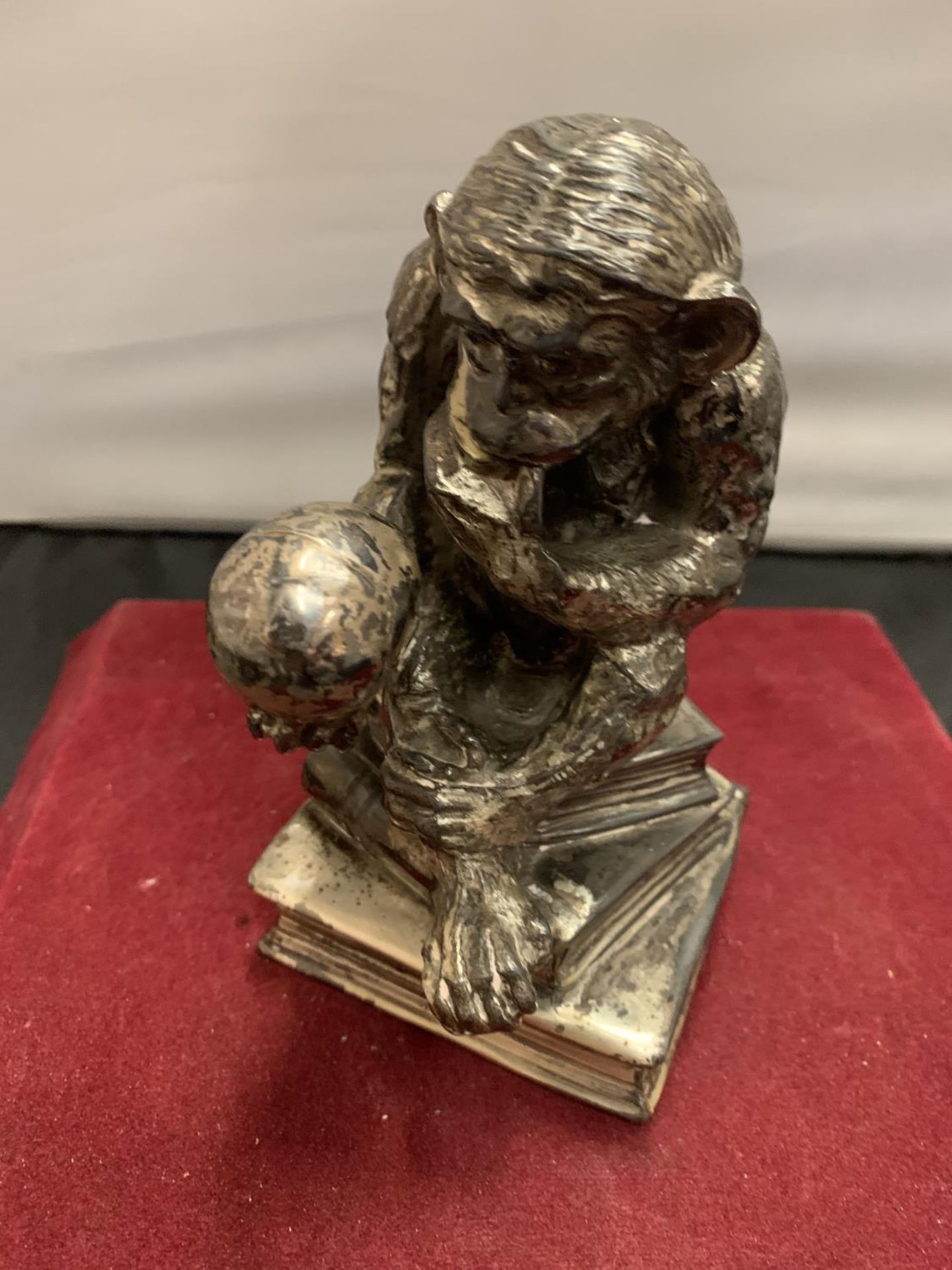 A CAST WHITE METAL TABLE LIGHTER IN THE FORM OF A MONKEY HOLDING A SKULL