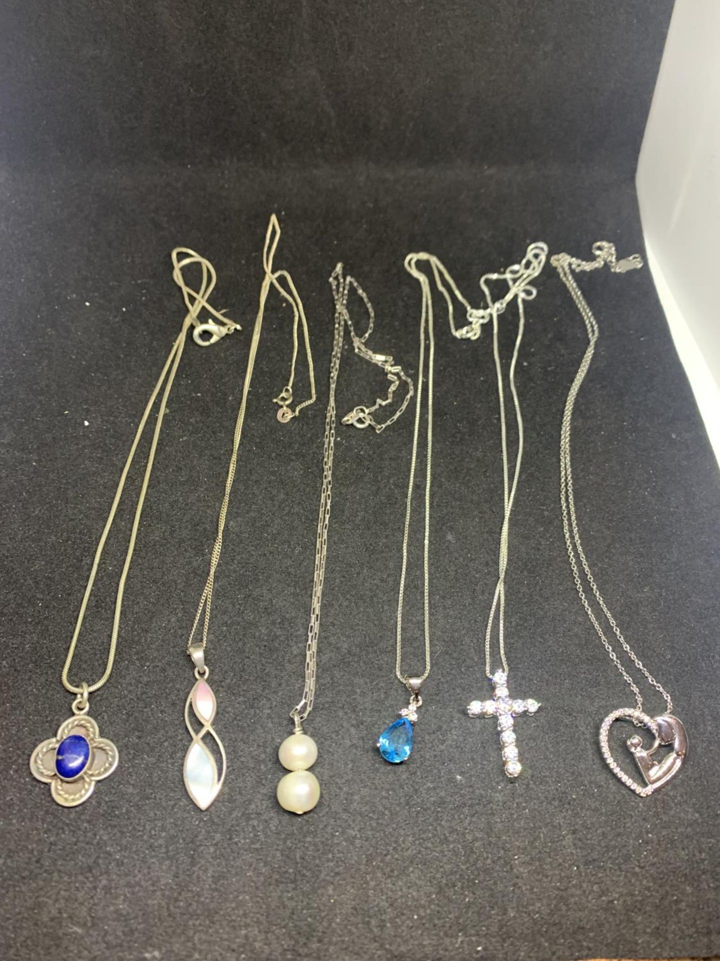 SIX MARKED SLIVER PENDANTS ON CHAINS TO INCLUDE A CLEAR STONE CROSS, HEART, BLUE STONE, PEARL ETC