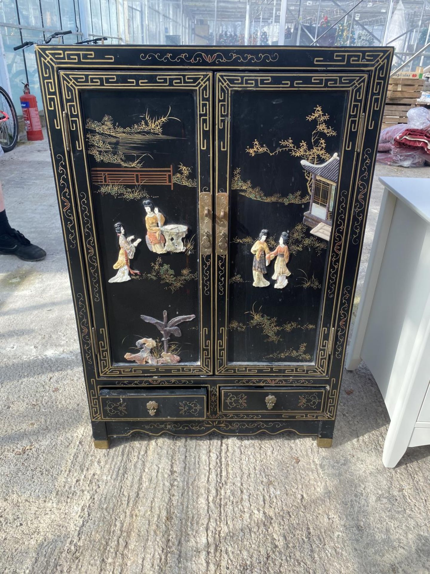 AN ORIENTAL BLACK LAQUER TWO DOOR CABINET WITH BASE DRAWERS, 24" WIDE WITH RAISED DECORATIONS