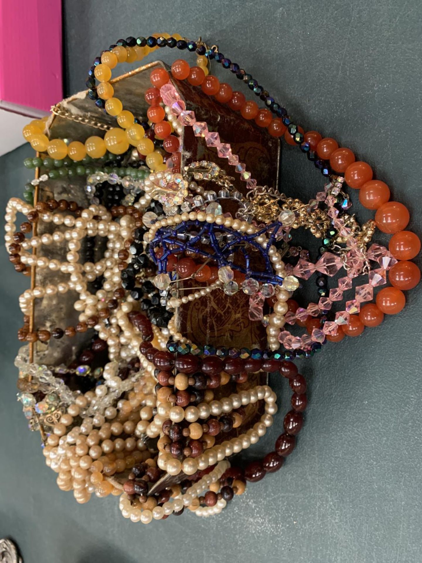 A VINTAGE TIN CONTAINING A QUANTITY OF COSTUME JEWELLERY TO MAINLY COMPRISE OF NECKLACES