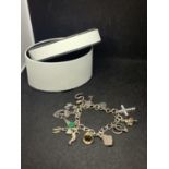 A SILVER CHARM BRACELET WITH ELEVEN CHARMS AND A HEART CLASP WITH A PRESENTATION BOX