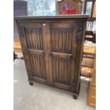 A REPRODUCTION OAK TWO DOOR CABINET WITH LINENFOLD DOORS 'GOODALLS FURNISHERS' MANCHESTER, 41.5"