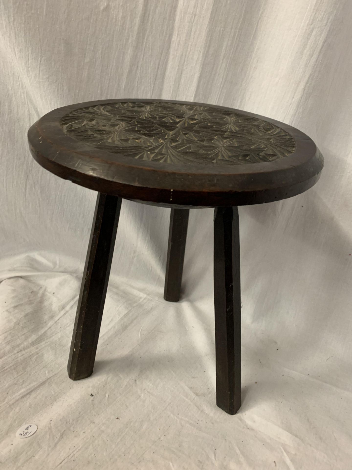 A SMALL THREE LEGGED HARD WOOD STOOL WITH CARVING TO THE SEAT H: 28.5CM