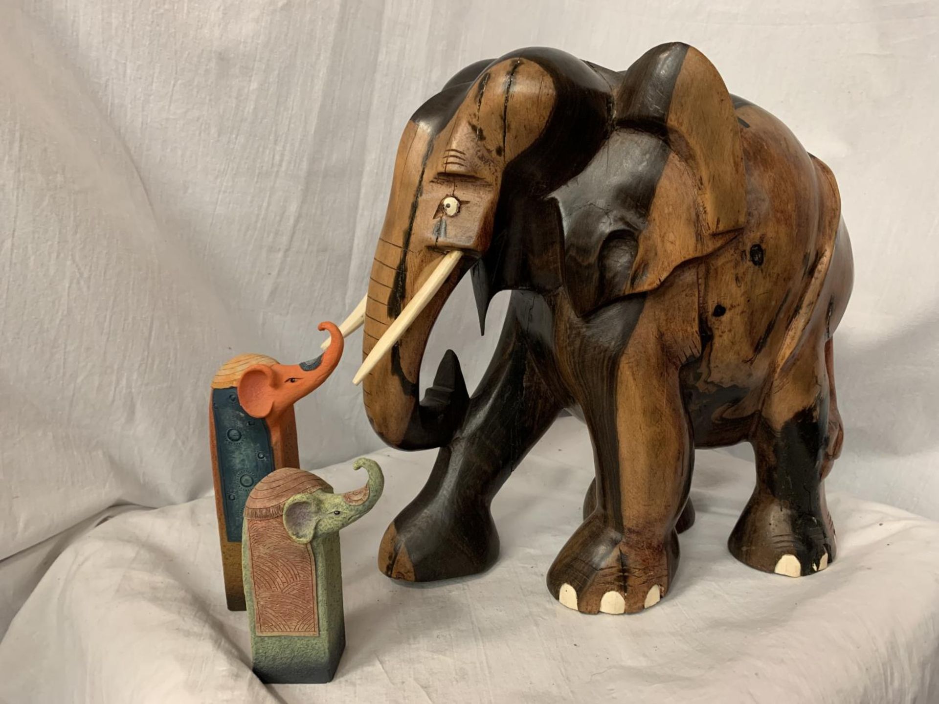 A LARGE CARVED HEAVY HARD WOOD ELEPHANT (H: APPROX. 30CM) AND TWO CERAMIC ELEPHANT ITEMS