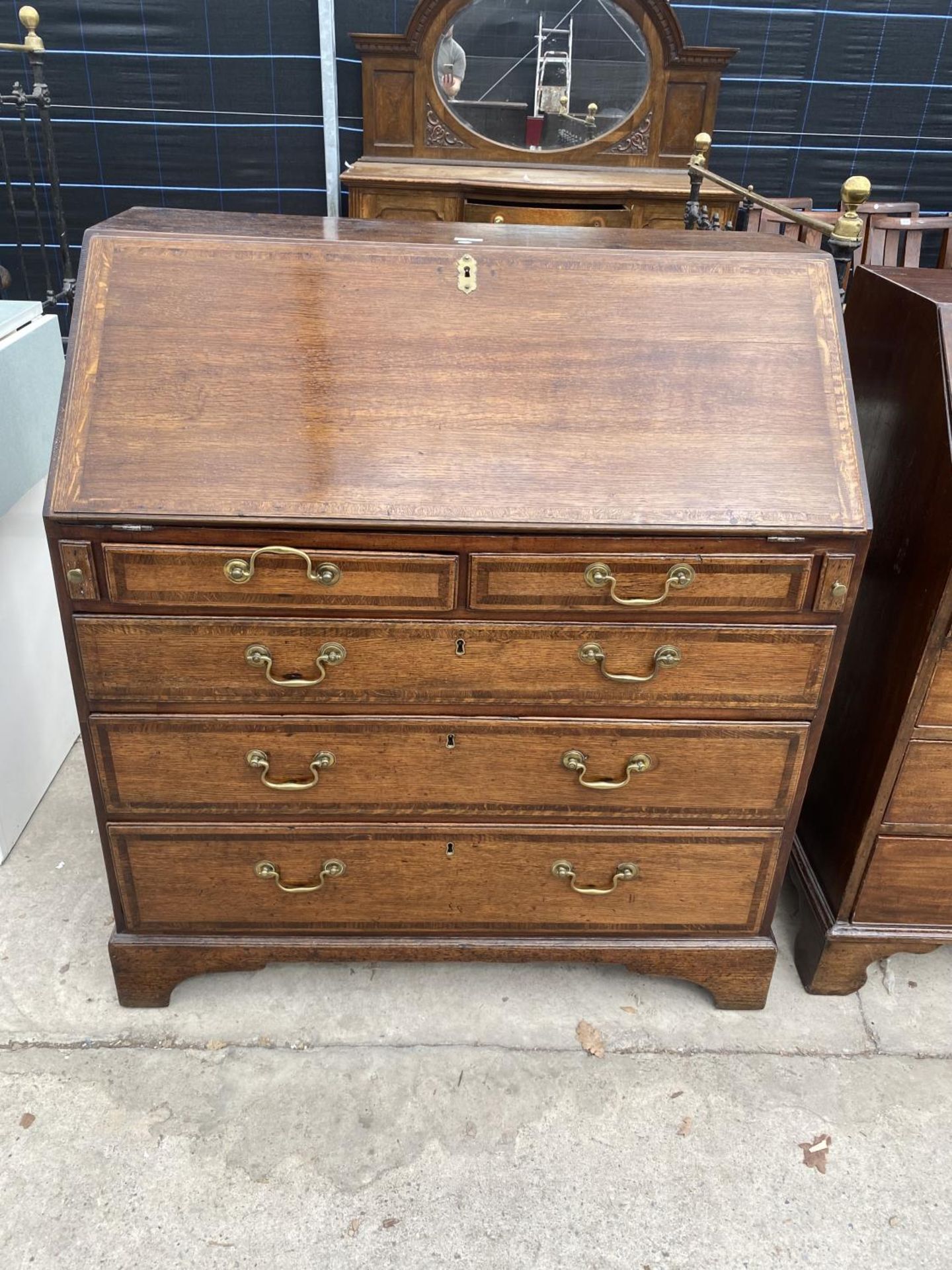 A GEORGE III OAK AND CROSSBANDED BUREAU WITH TWO SHORT AND THREE GRADUATED DRAWERS ON BRACKET FEET