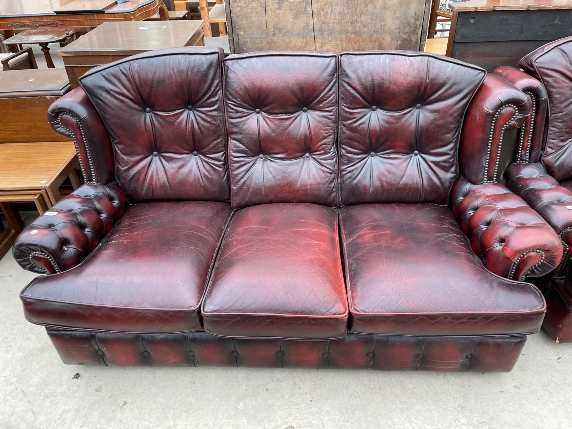 AN OXBLOOD LEATHER THREE SEATER SOFA WITH BUTTONED BACK AND ARMS