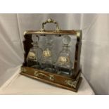 AN ANTIQUE VICTORIAN OAK TANTALUS TO INCLUDE THREE CUT GLASS DECANTERS (RIM A/F) WITH THREE MARKED