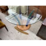 A MODERNIST CIRCULAR GLASS TOP TABLE SUPPORTED BY SIX COLOURED TUSK SHAPED LEGS, ON PLATEAU BASE,