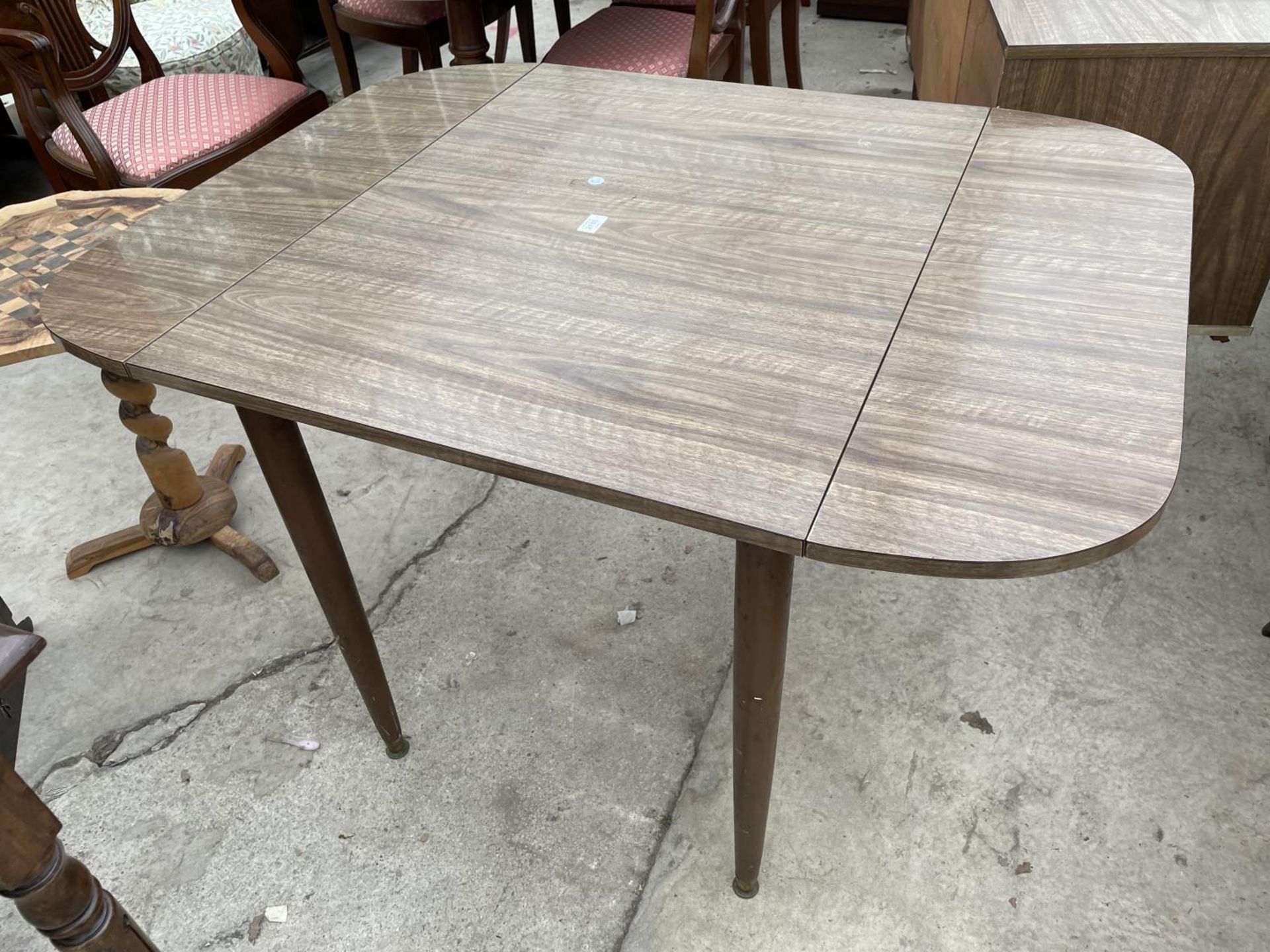 A 1950'S CREAMY WALNUT EFFECT DROP-LEAF DINING TABLE ON TAPERED LEGS