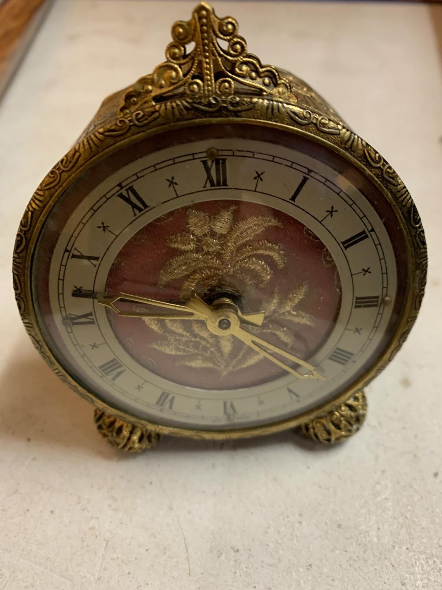 A VINTAGE ORNATE GILT ALARM CLOCK WITH EMBRIODERED FACE