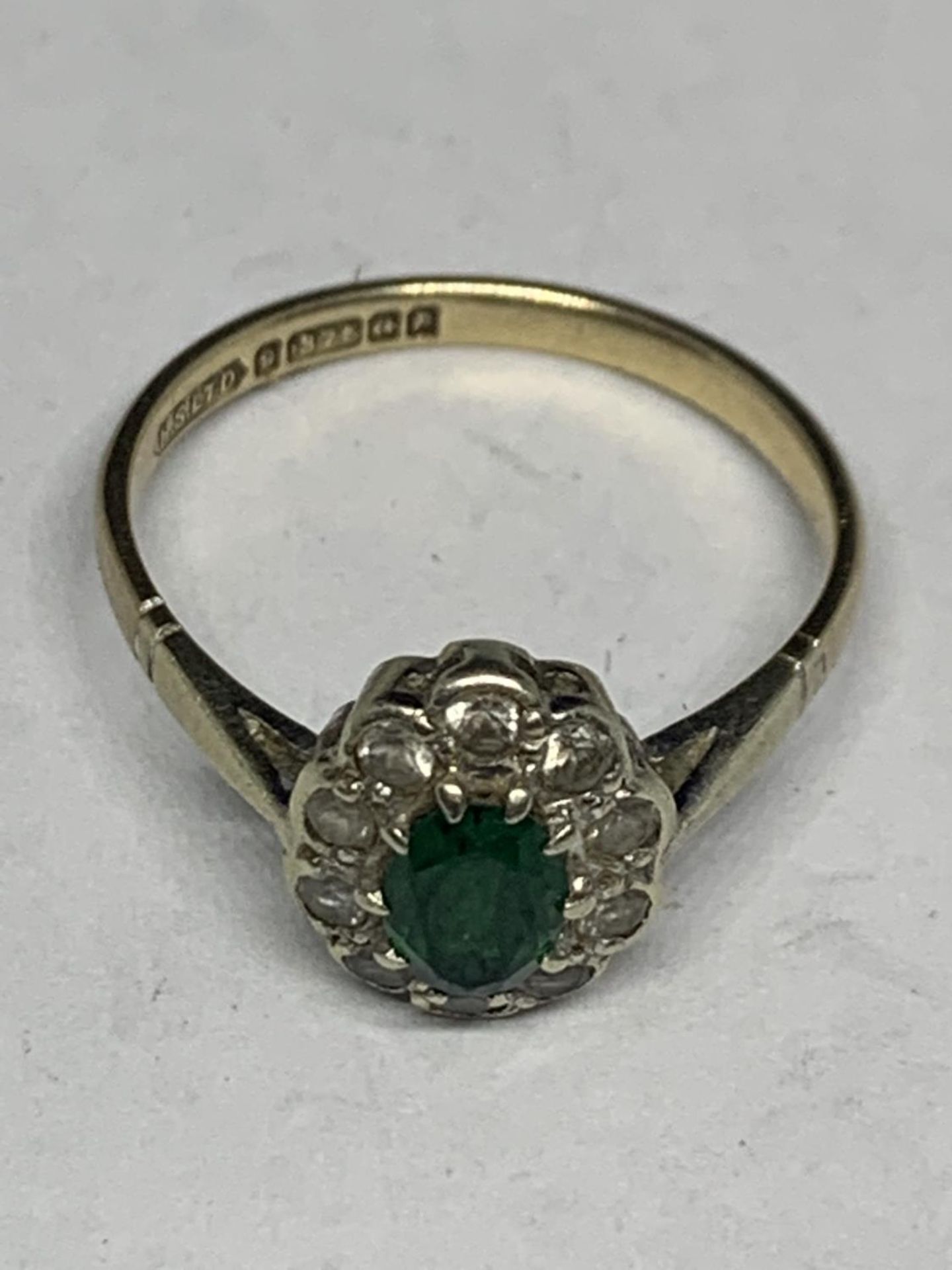 A 9 CARAT GOLD RING WITH A GREEN CENTRE STONE AND CLEAR STONE SURROUNDS SIZE M/N