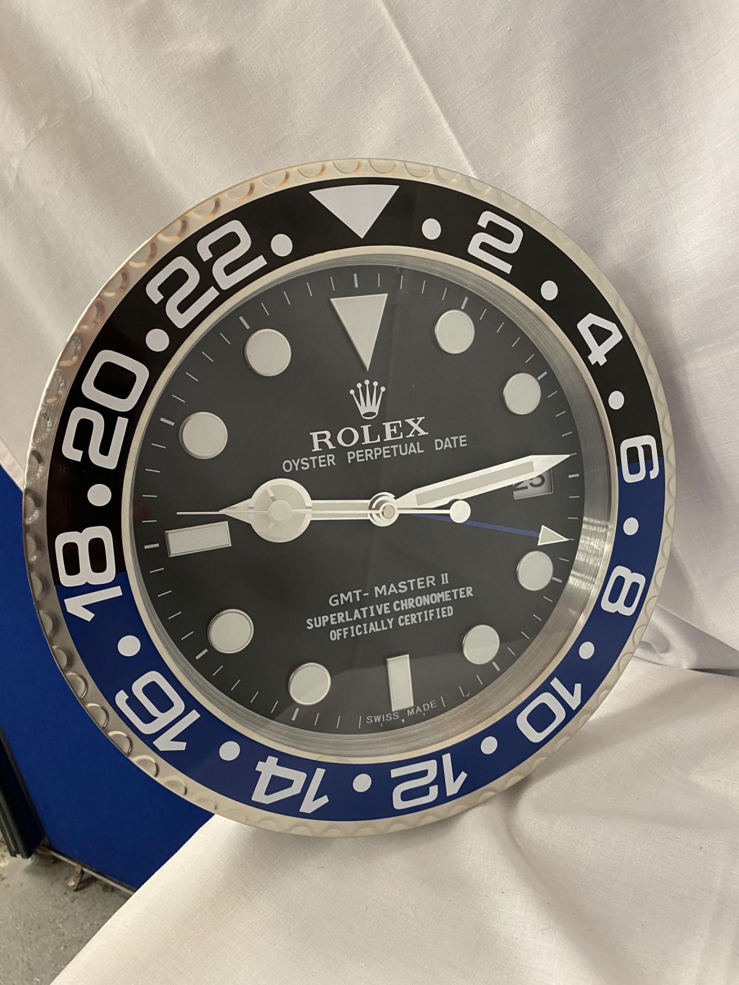 A METAL SILVER AND BLUE WALL CLOCK DIPICTING A ROLEX OYSTER FACE