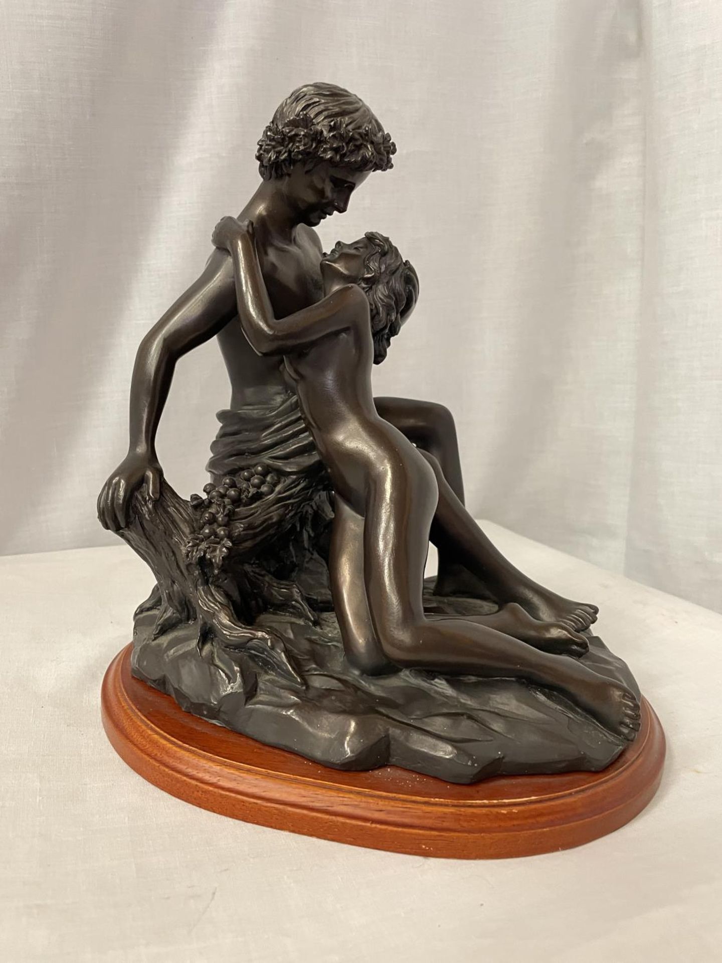A BRONZE STYLE ORNAMENT OF AN EMBRACING COUPLE ON WOODEN STAND, HEIGHT 27CM