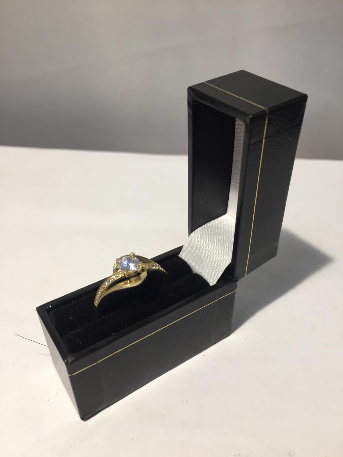 A 9 CARAT GOLD RING WITH A CLEAR STONE SOLITAIRE AND CLEAR STONES ON THE SHOULDERS WITH PRESENTATION