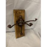 A CAST METAL THREE COAT/HAT HOOKS MOUNTED ON WOODEN WALL PLINTH