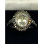 A CONTINENTAL WHITE AND YELLOW METAL RING WITH CENTRE DIAMOND AND SMALLER SURROUNDING DIAMONDS WHICH