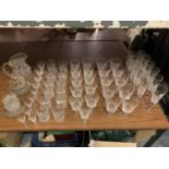 A LARGE QUANTITY OF GLASSWARE TO INCLUDE TUMBLERS, CHANPAGNE GLASSES AND A JUG