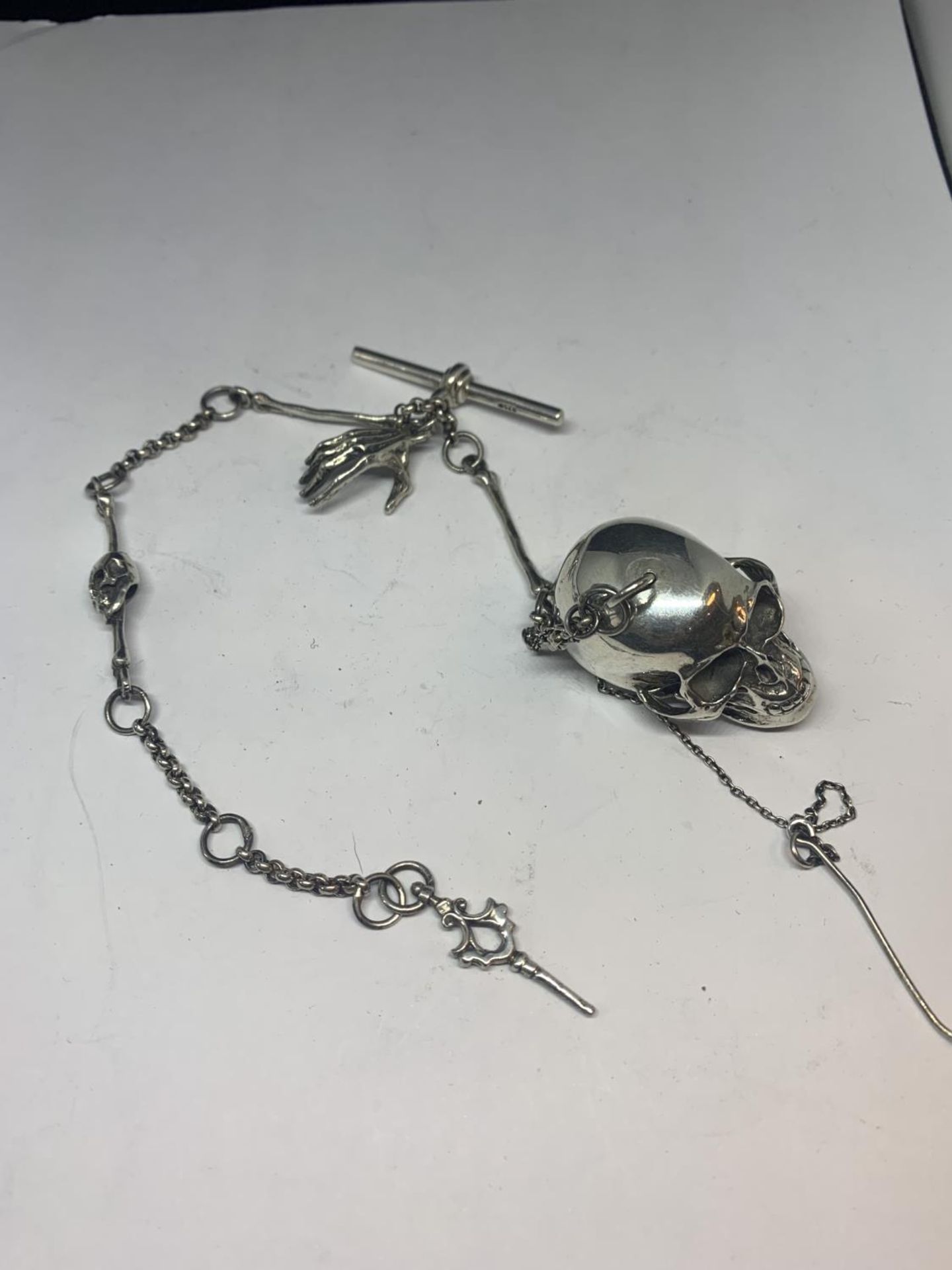 A HEAVY SILVER ALBERT CHAIN WITH LARGE SKULL FOB AND BONE, HAND ETC DESIGN