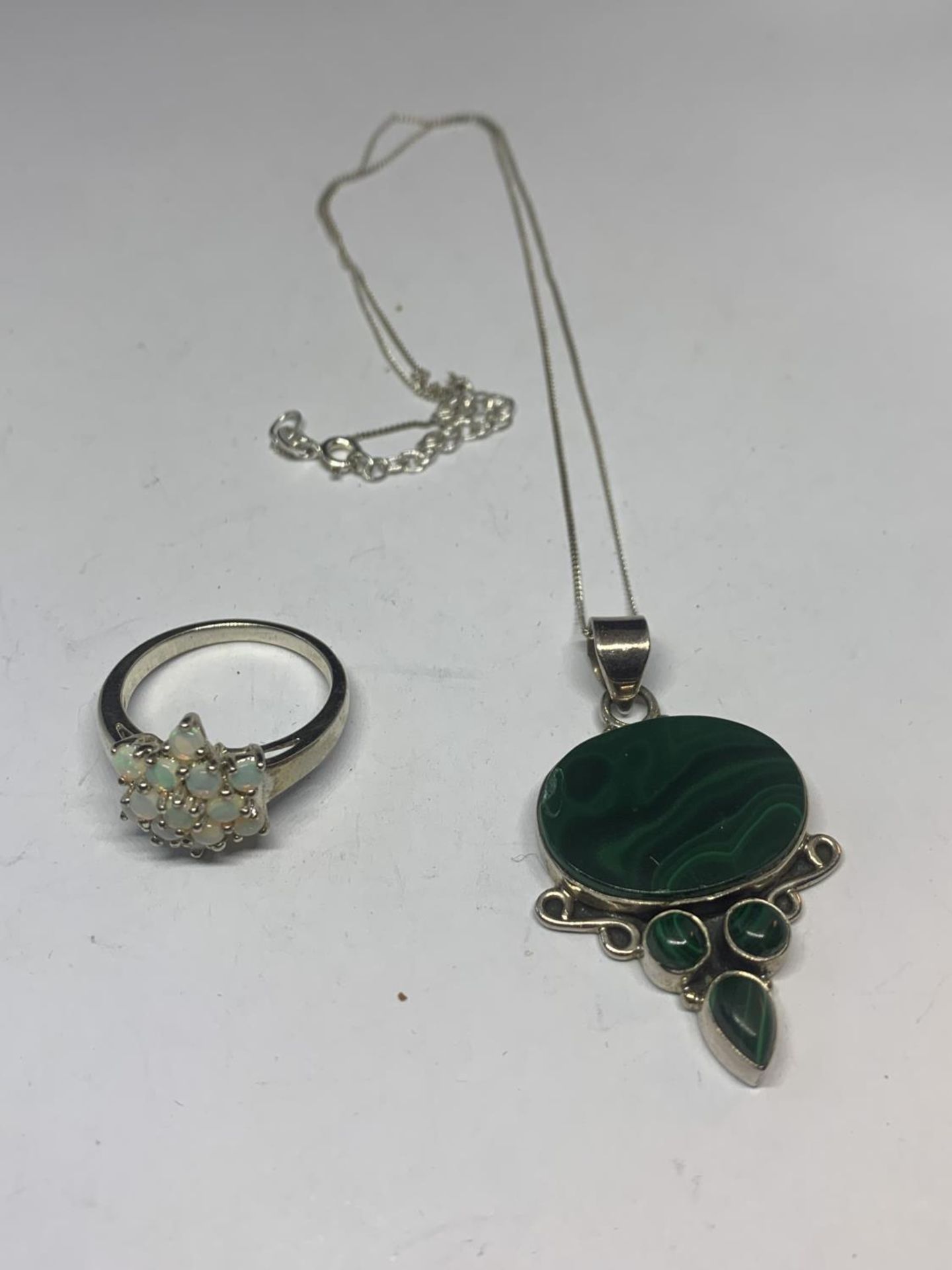 A SILVER NECKLACE WITH A GREEN STONE PENDANT AND A RING IN A FLOWER DESIGN WITH A PRESENTATION BOX