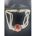 A THREE STRAND PEARL NECKLACE WITH A GILT CHOKER WITH LARGE RED STONE