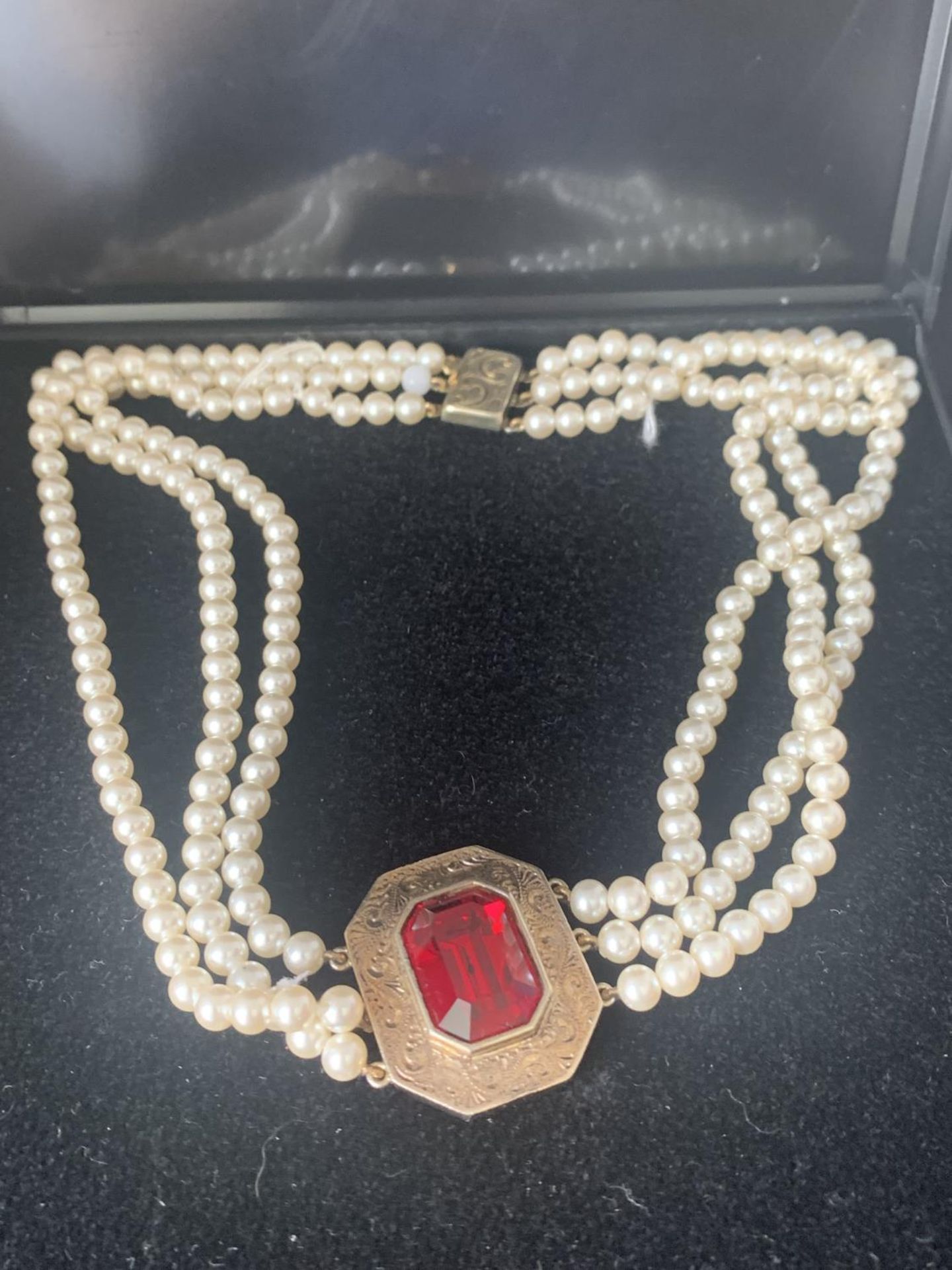 A THREE STRAND PEARL NECKLACE WITH A GILT CHOKER WITH LARGE RED STONE