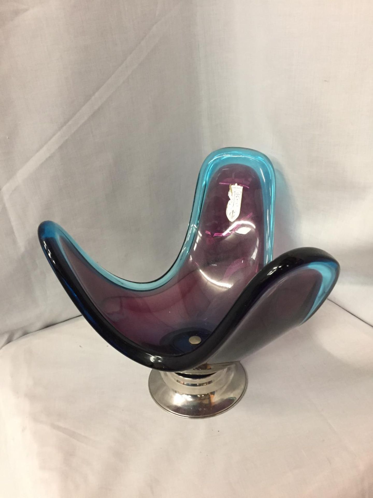 A PURPLE AND TURQUOISE GLASS ABSTRACT DESIGN DISH ON A WHITE METAL STAND