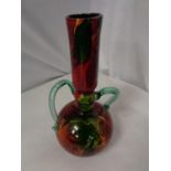 A RED GLASS VASE WITH GREEN HANDLES