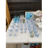 A LARGE QUANTITY OF COLOURED GLASS WARE TO INCLUDE TUMBLERS, FLUTES AND A JUG ETC