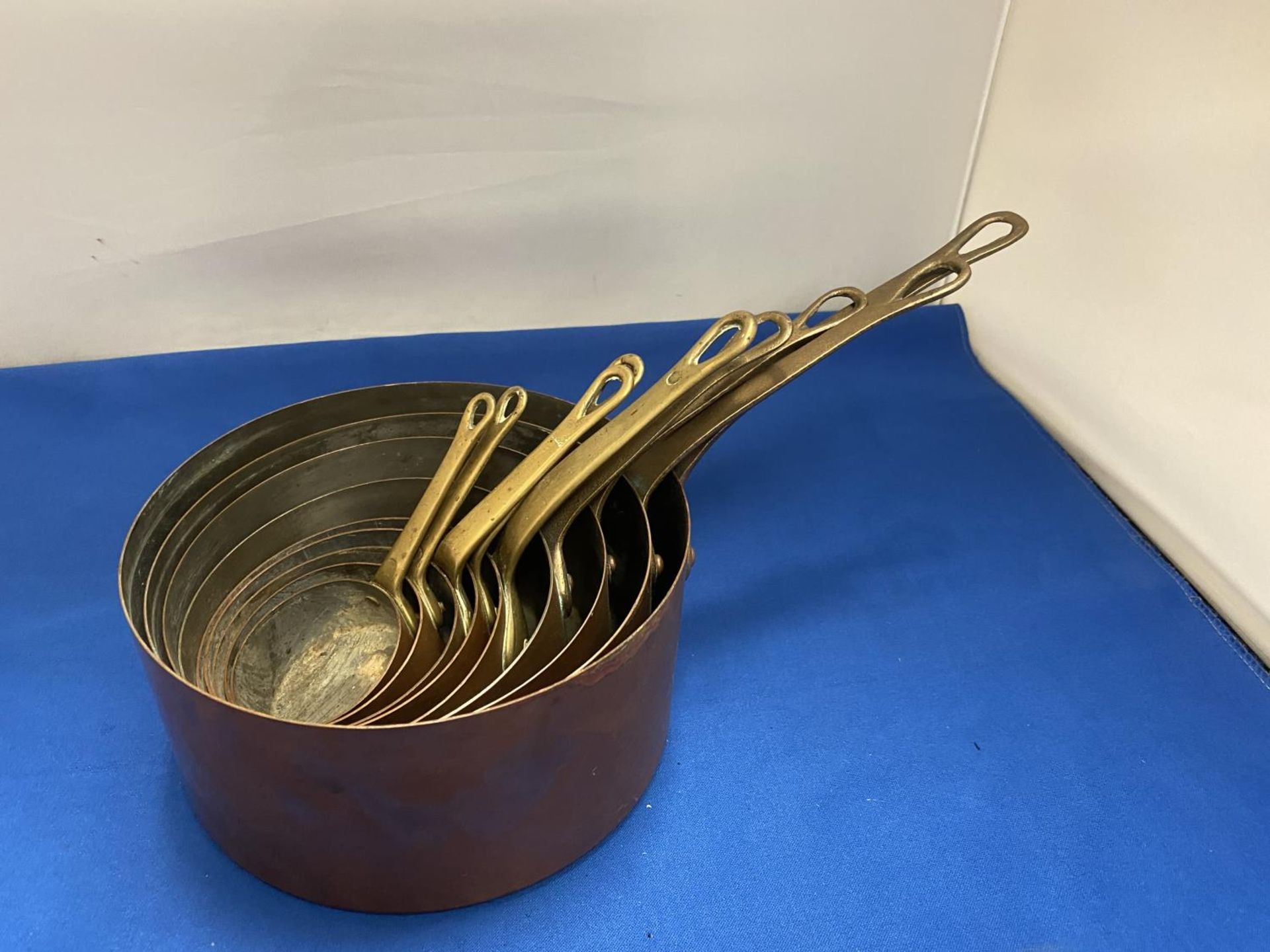 A SET OF NINE COPPER GRADUATED PANS WITH BRASS HANDLES