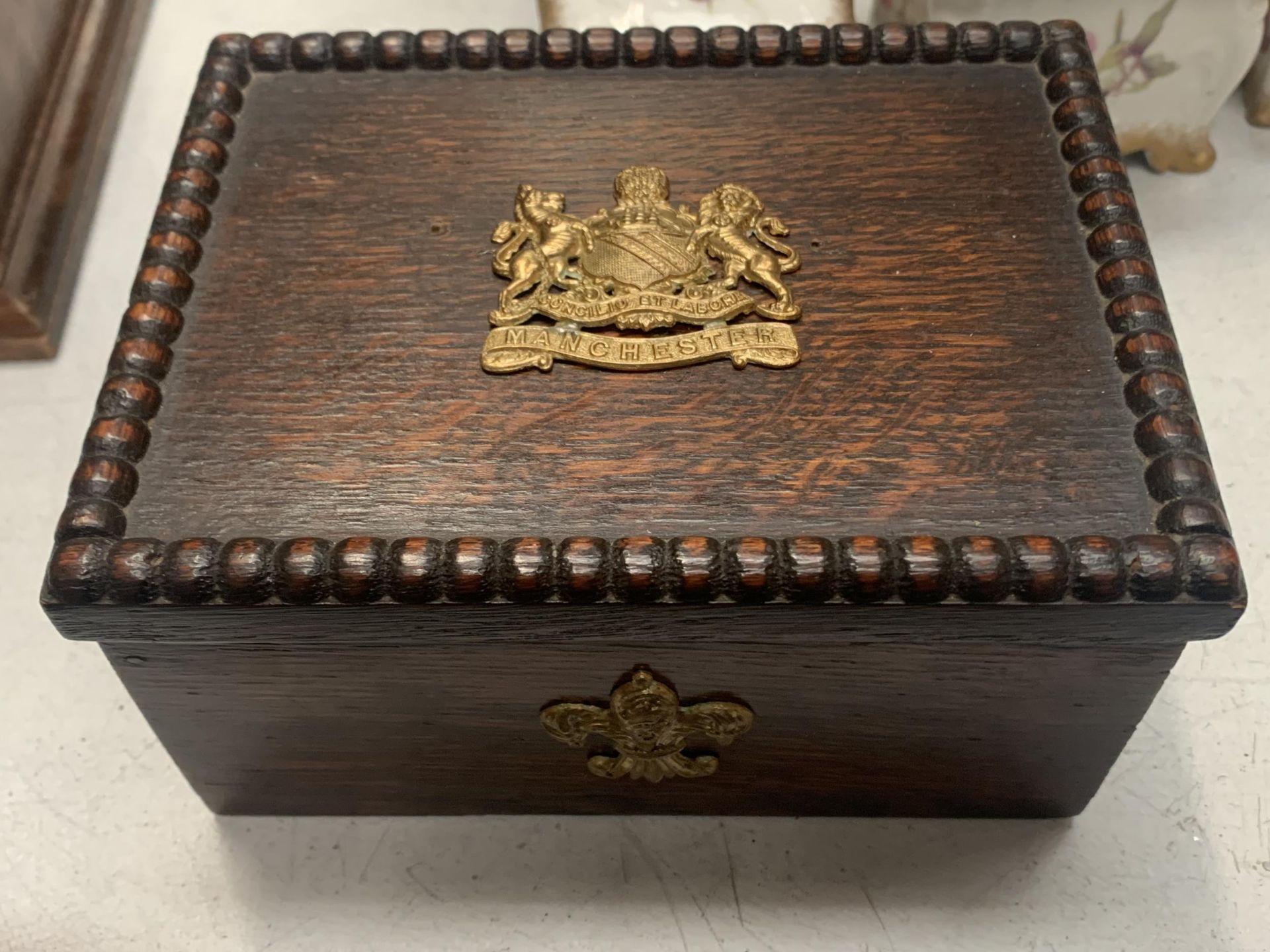AN ORNATE WOODEN BOX WITH THE MANCHESTER COAT OF ARMS TO THE LID IN YELLOW METAL AND A FURTHER WHEAT