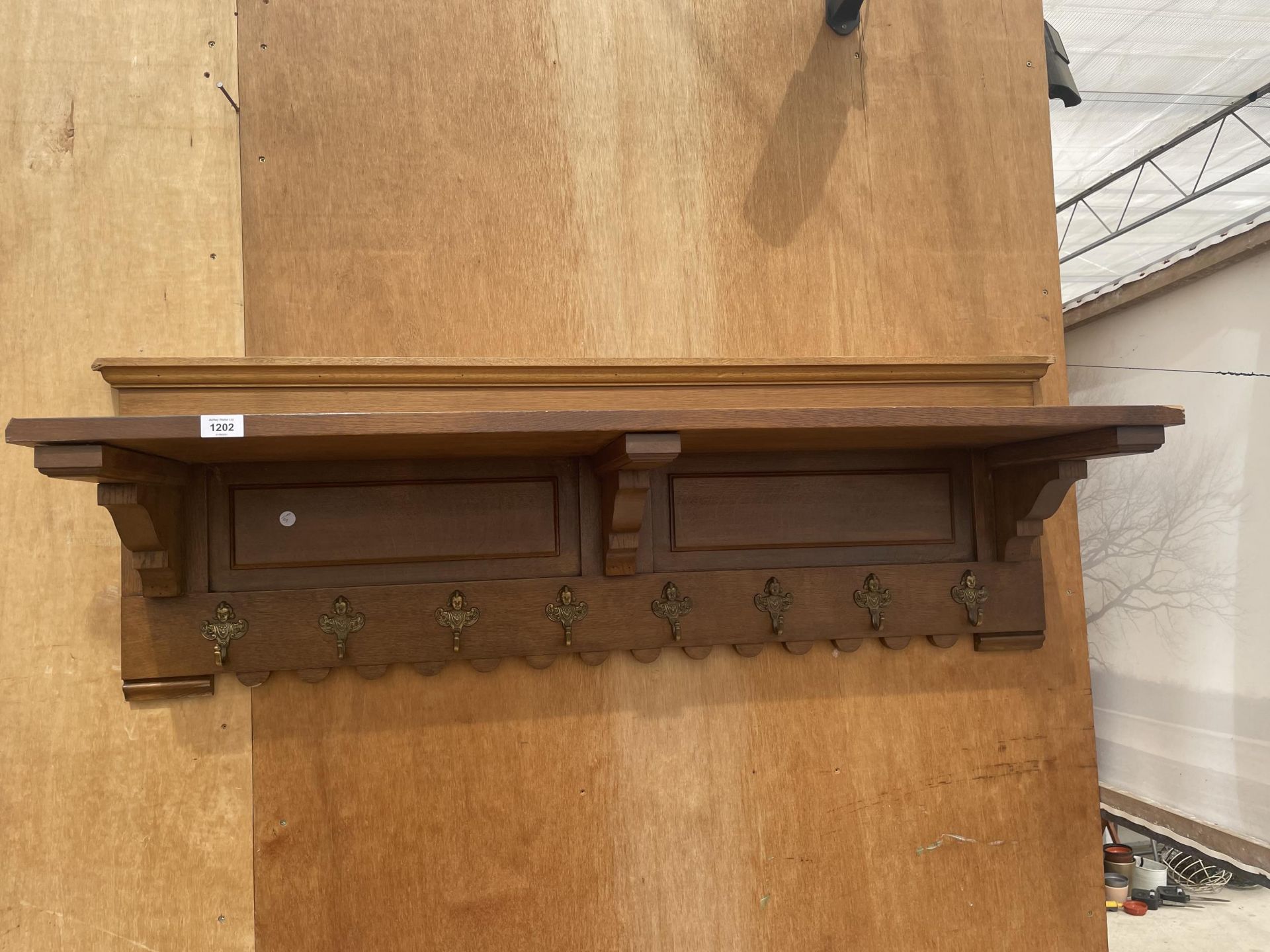 AN EARLY 20TH CENTUARY OAK HALL SHELF INCORPORATING EIGHT DECORATIVE BRASS COAT HOOKS