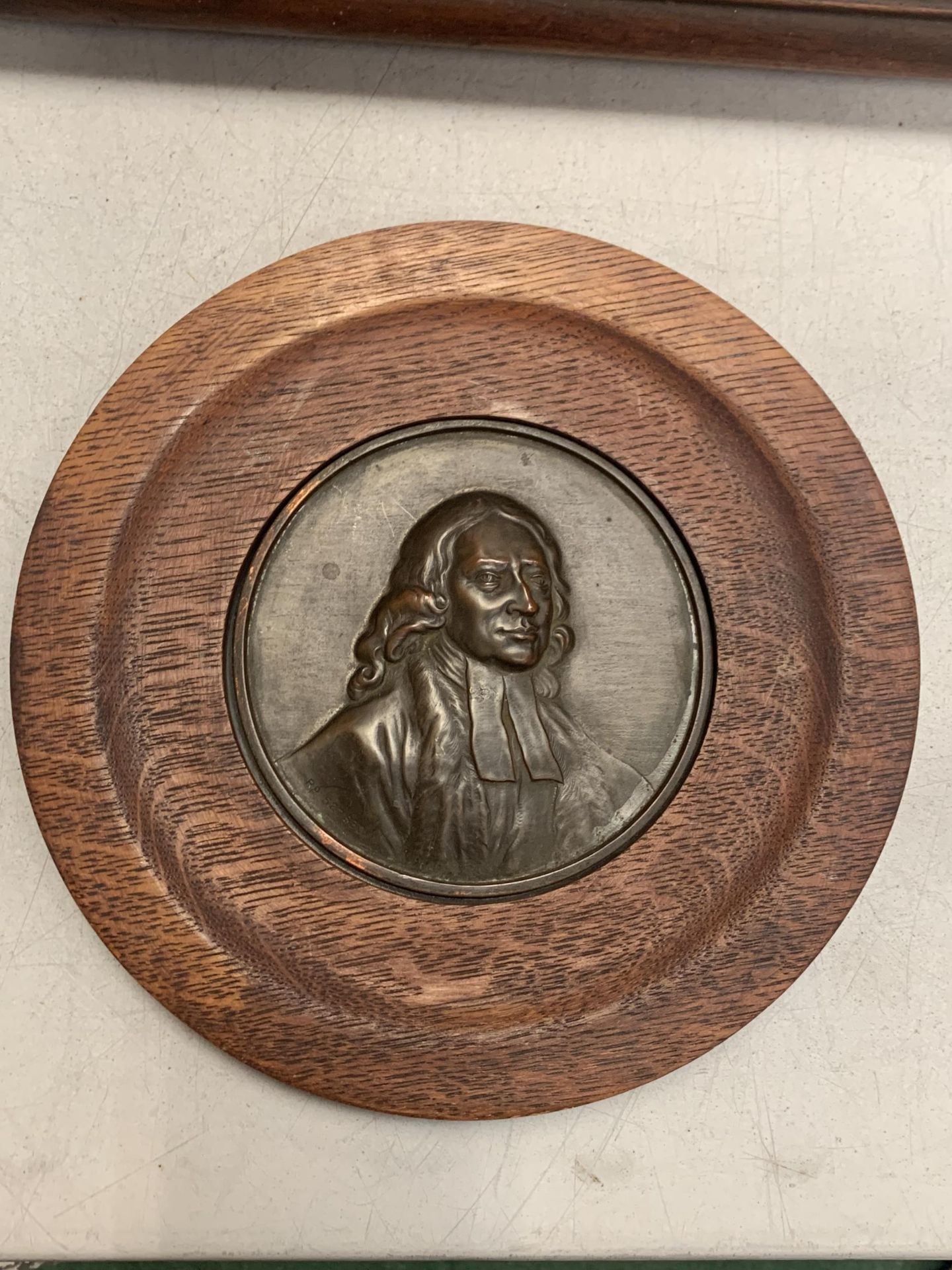 A CIRCULAR BRASS PLAQUE DEPICTING A GENTLEMAN WITH A WOODEN SURROUND