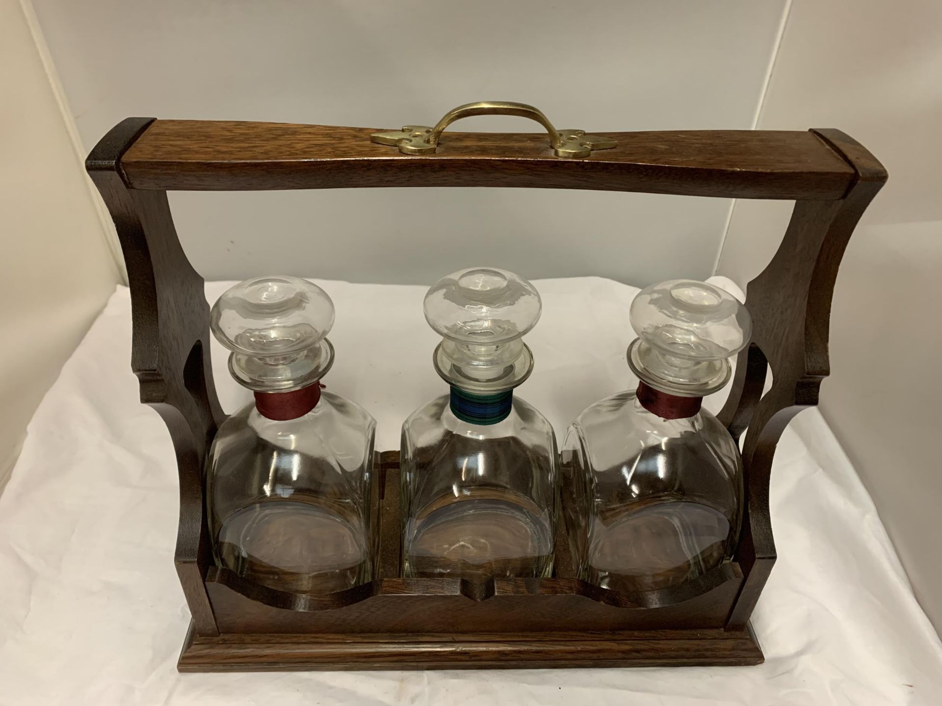 AN OAK WITH BRASS HANDLE TANTALUS WITH THREE DECANTERS