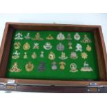 A GLAZED DISPLAY CASE CONTAINING THIRTY ONE BRITISH ARMY CAP BADGES, 29CM X 47CM