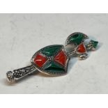 A SILVER BROOCH WITH GREEN AND RED ENAMEL AXE AND SHIELD DESIGN